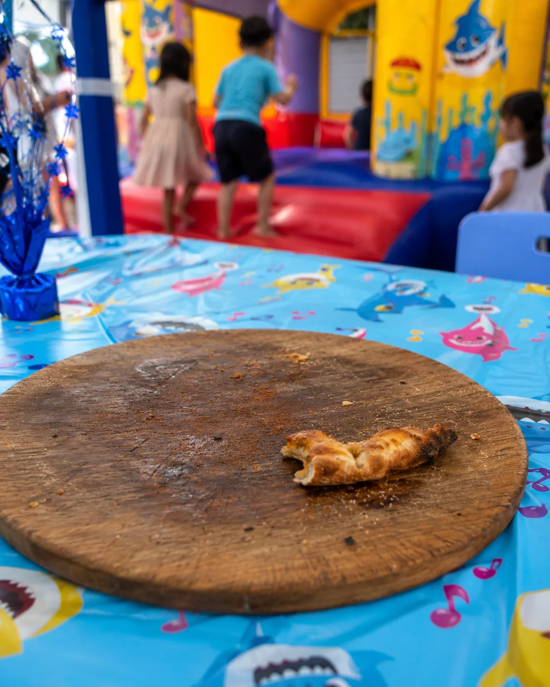 Cumpleaños con castillo inflable al fondo; en la mesa solo quedó el borde de la pizza