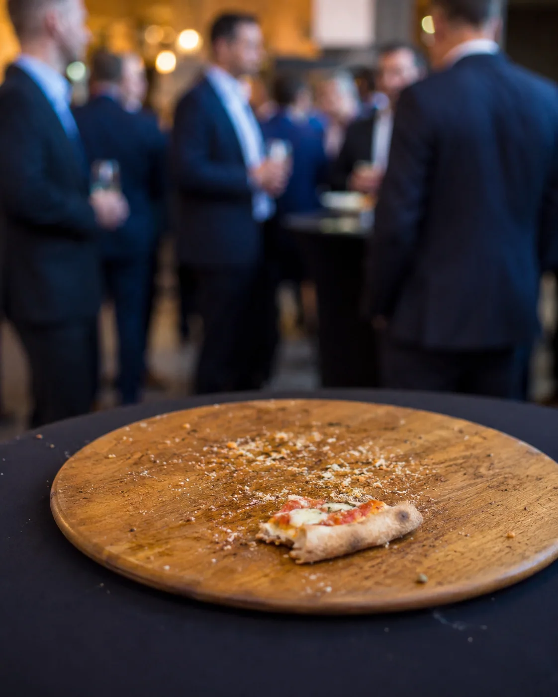 Evento de empresa: gente de traje conversando y en la mesa la última porción de pizza